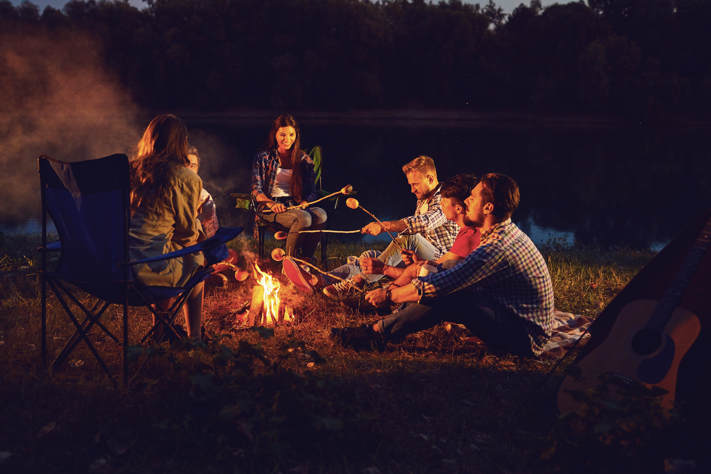 a group of adults sit around a roaring fire in the woods roasting marshmallows!